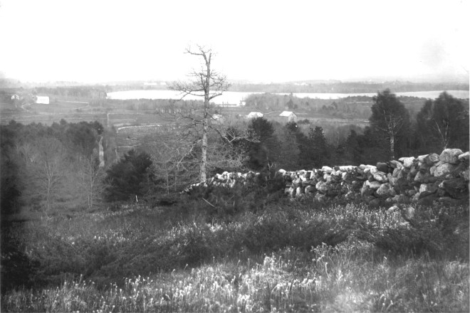 A tall stone wall divides a field on Dinsmoor Hill, Windham with Canobie lake in background. 